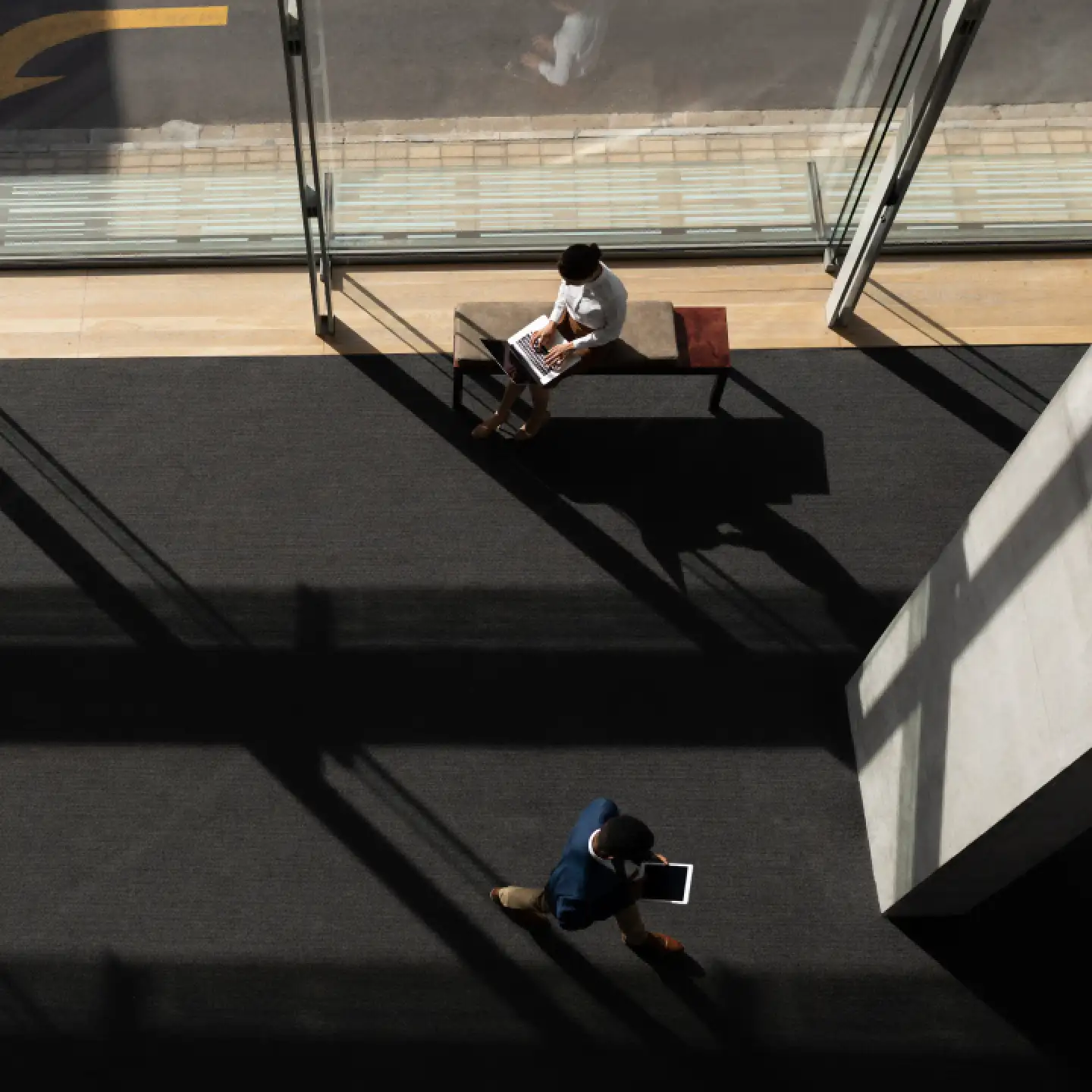 Arial view of a sleek and modern lobby where one person is sitting and using a laptop and another person is walking by.