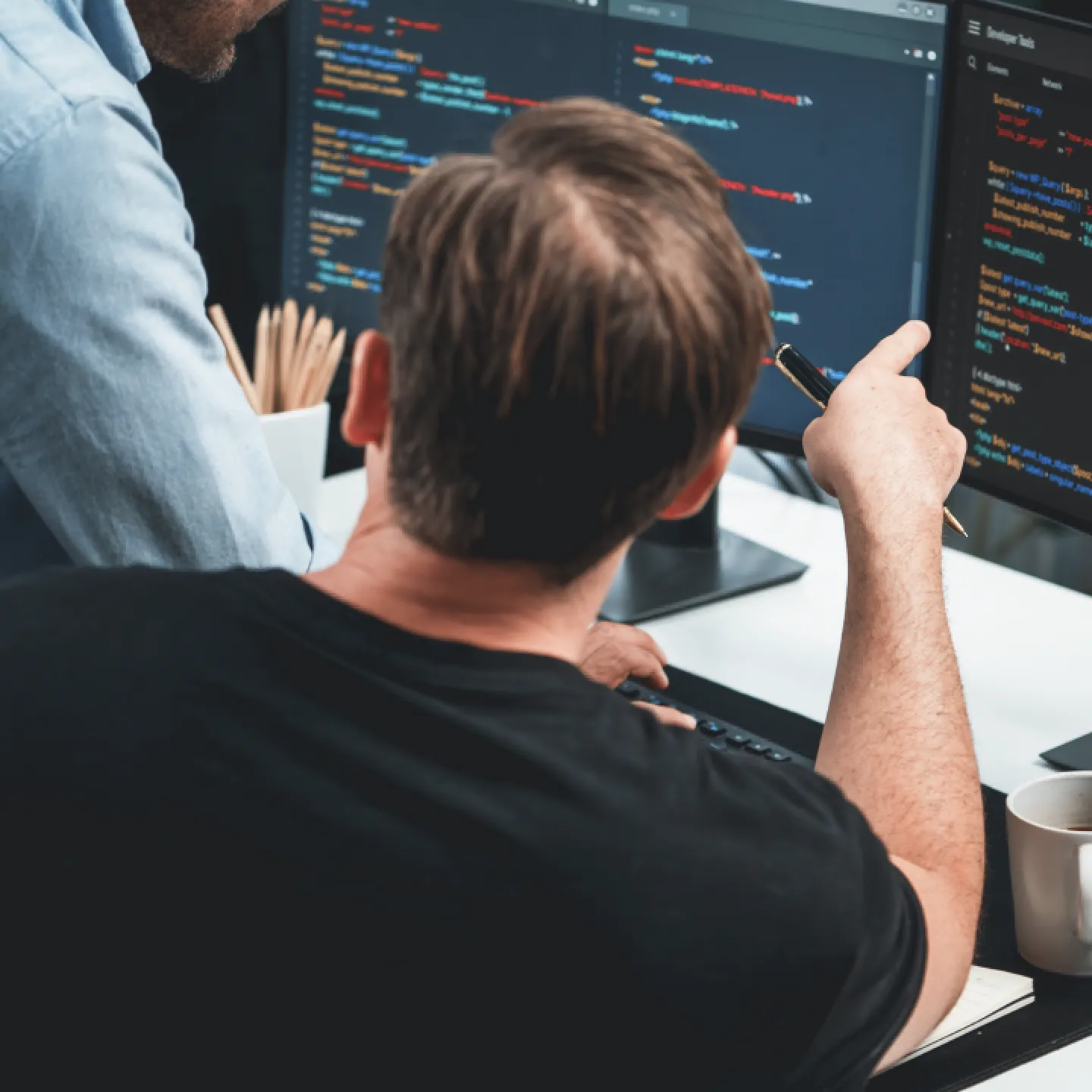 Person pointing at a computer screen with coding being shown. Two people collaborating on coding.