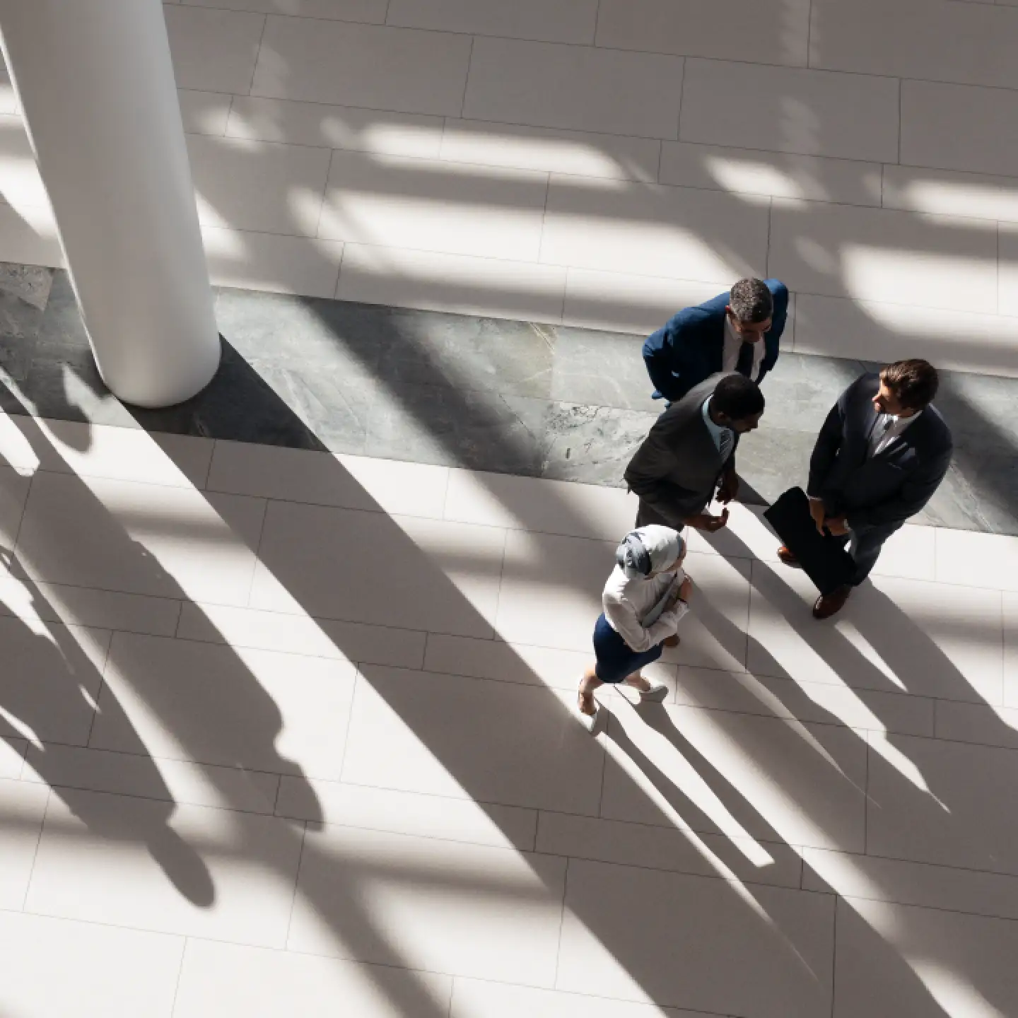 A group of professionals conversing in a corporate building lobby filled with natural light.